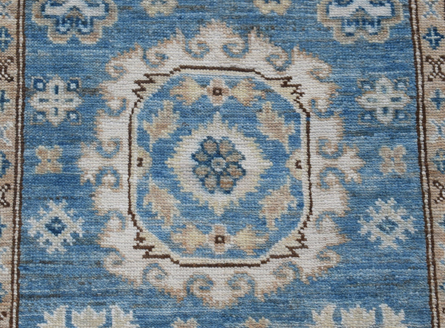 An Afghan Super Kazakh runner rug featuring a blue field with traditional cream floral motifs.