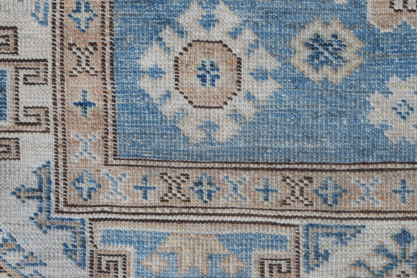 A close-up of an Afghan Super Kazakh runner featuring traditional blue and beige geometric motifs.