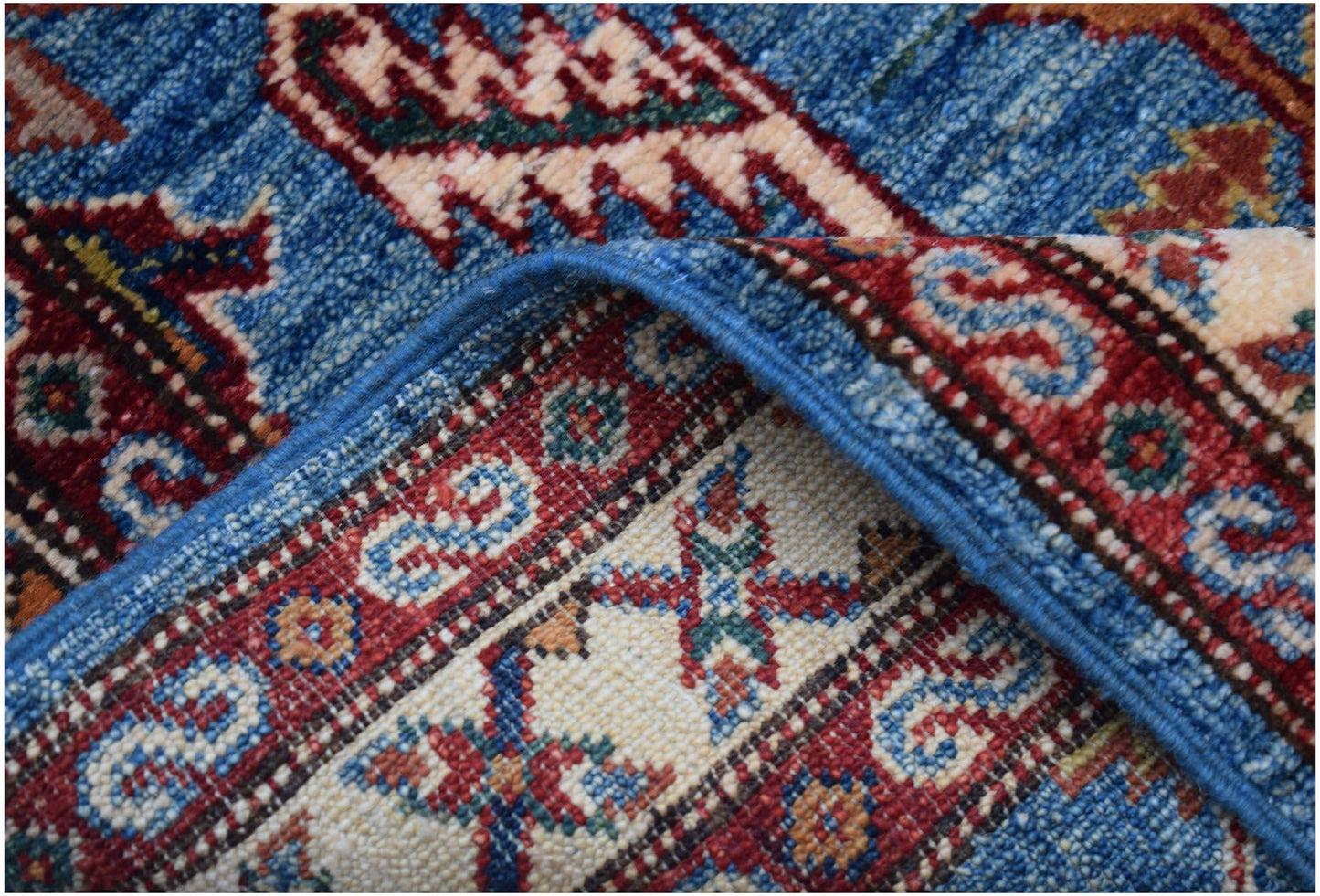 A close-up of a handmade Afghan Super Kazakh runner featuring traditional blue and red patterns.