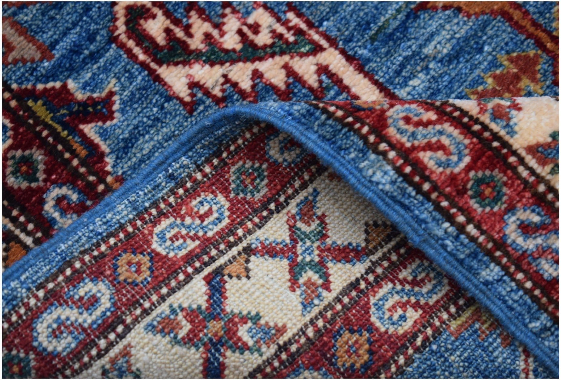 A close-up of a handmade Afghan Super Kazakh runner featuring traditional blue and red patterns.