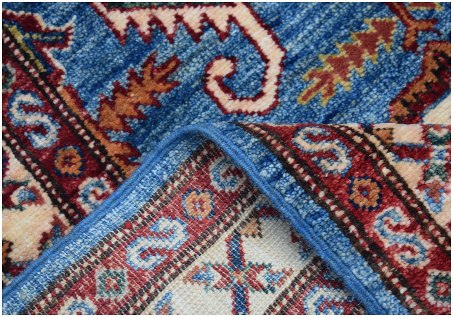 A close-up view of a handmade Afghan Super Kazakh runner featuring traditional blue, red, and cream geometric patterns.