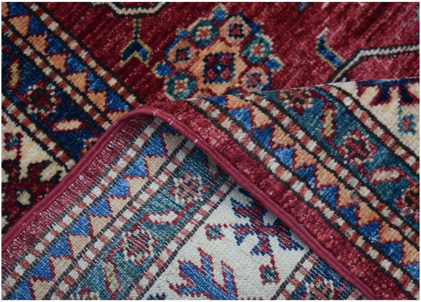 A close-up of a handmade Afghan Super Kazakh runner featuring traditional geometric motifs in red, blue, and cream wool.