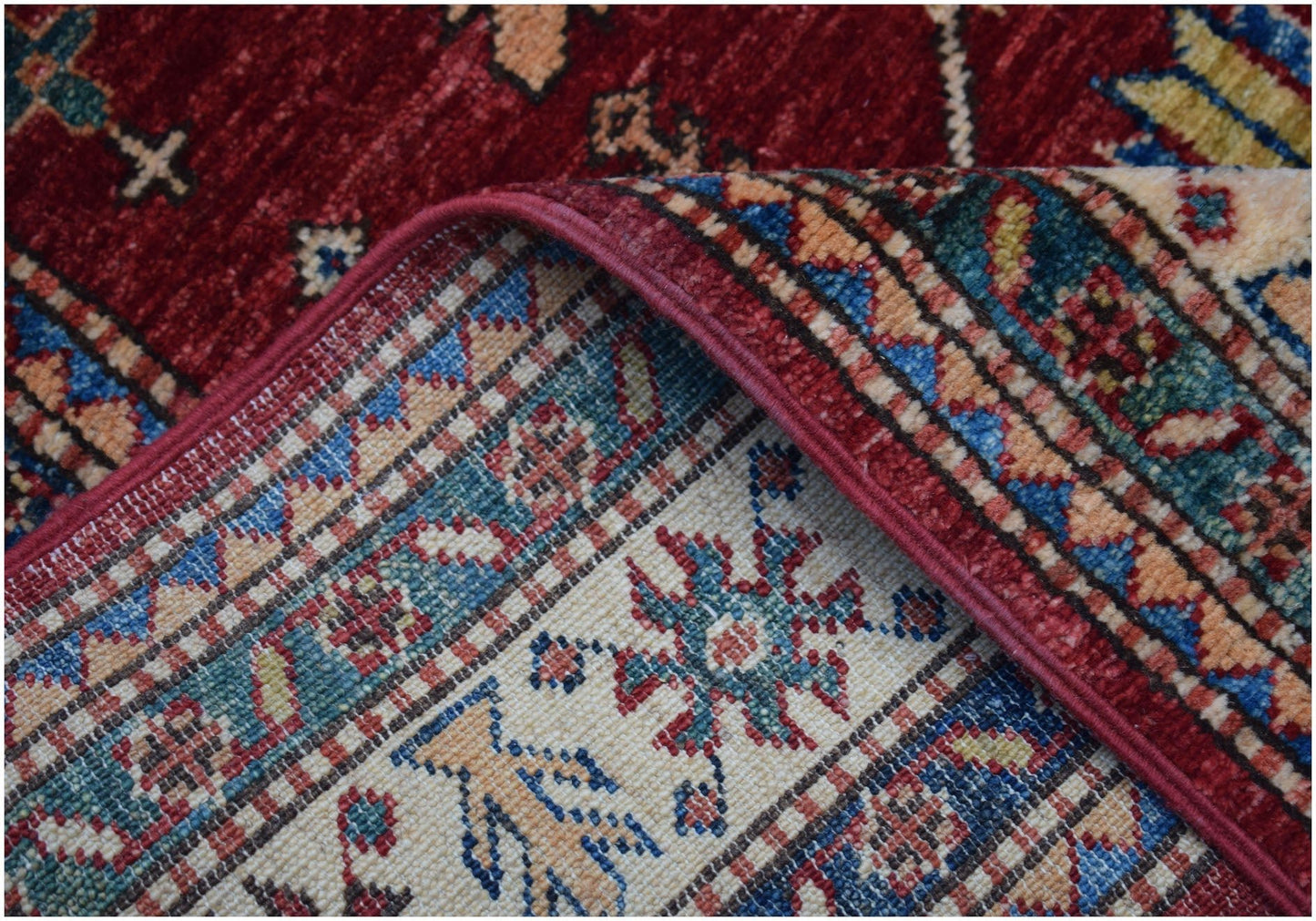A corner of a handmade Afghan Super Kazakh runner featuring traditional red, blue, and cream motifs.
