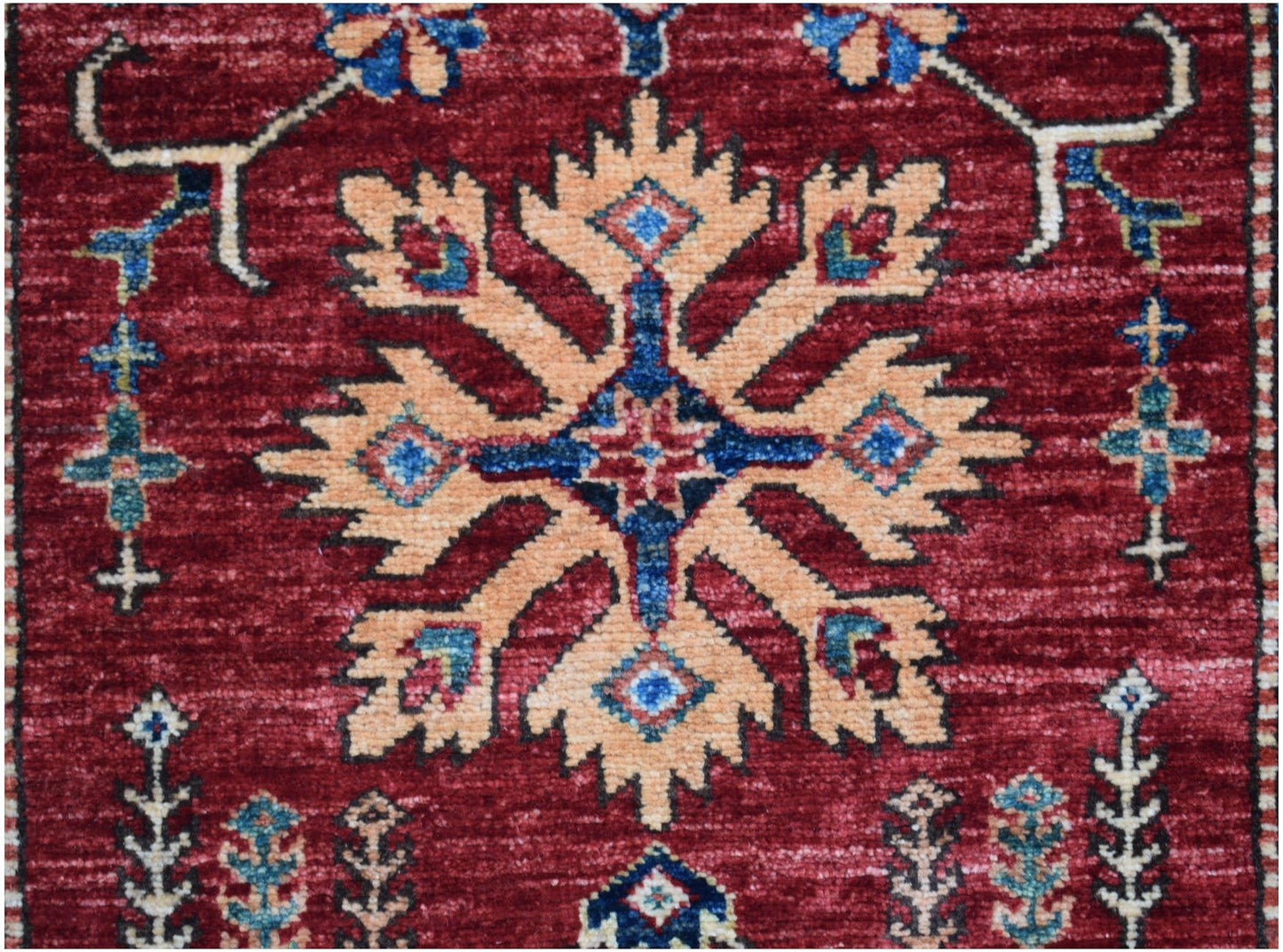 An Afghan Super Kazakh runner featuring a central geometric floral motif on a deep red background.