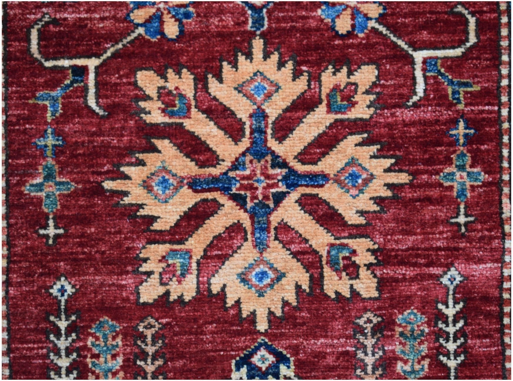 An Afghan Super Kazakh runner featuring a central geometric floral motif on a deep red background.