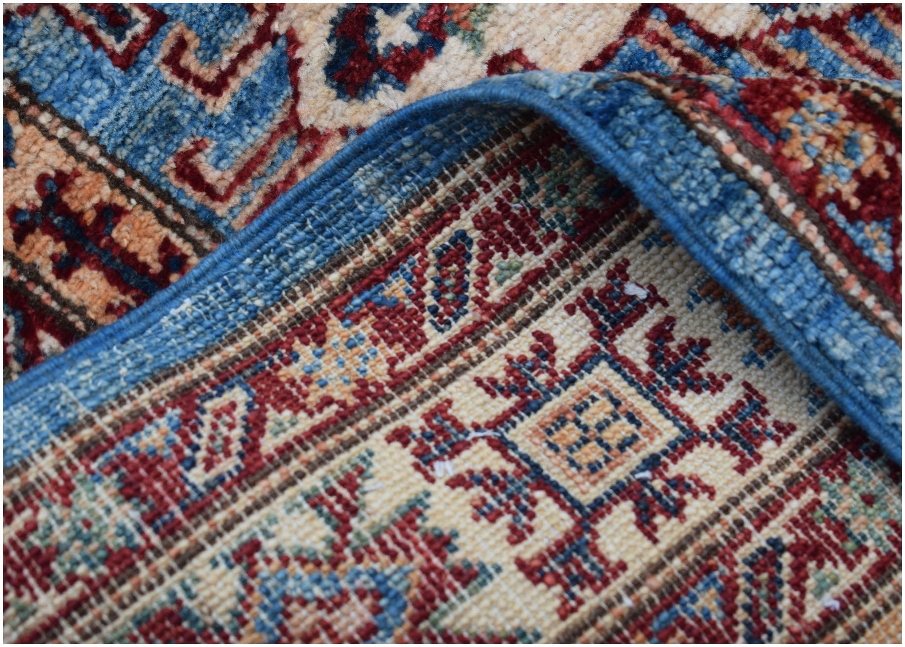 A close-up view of a handmade Afghan Super Kazakh runner featuring traditional red and blue motifs.
