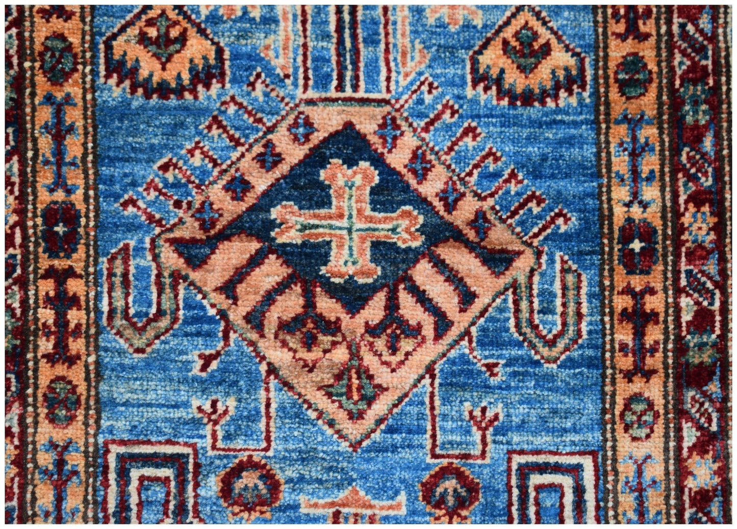 A handmade Afghan Super Kazakh runner featuring a central cross motif on a blue wool background.
