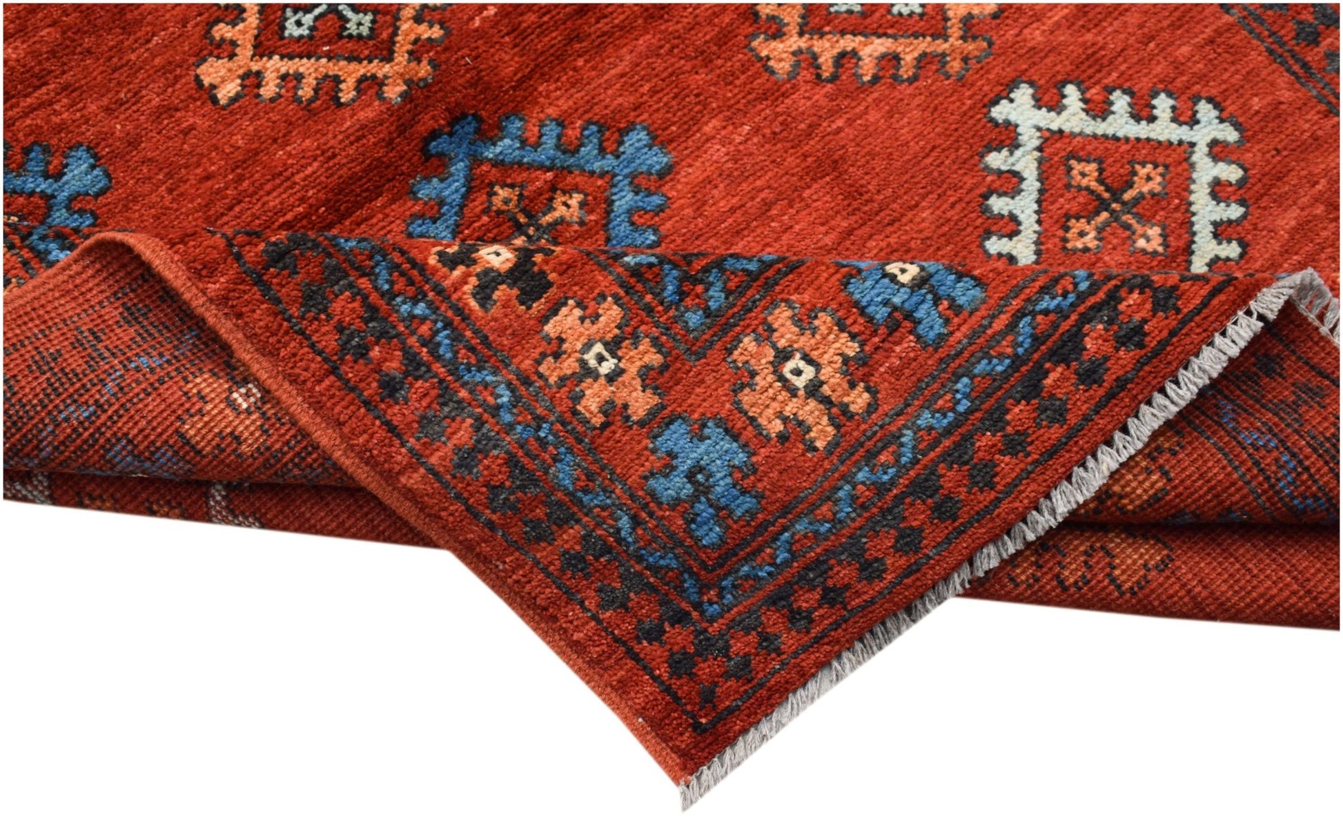 A handwoven Afghan Pashm rug featuring a red field with geometric patterns and a folded corner.