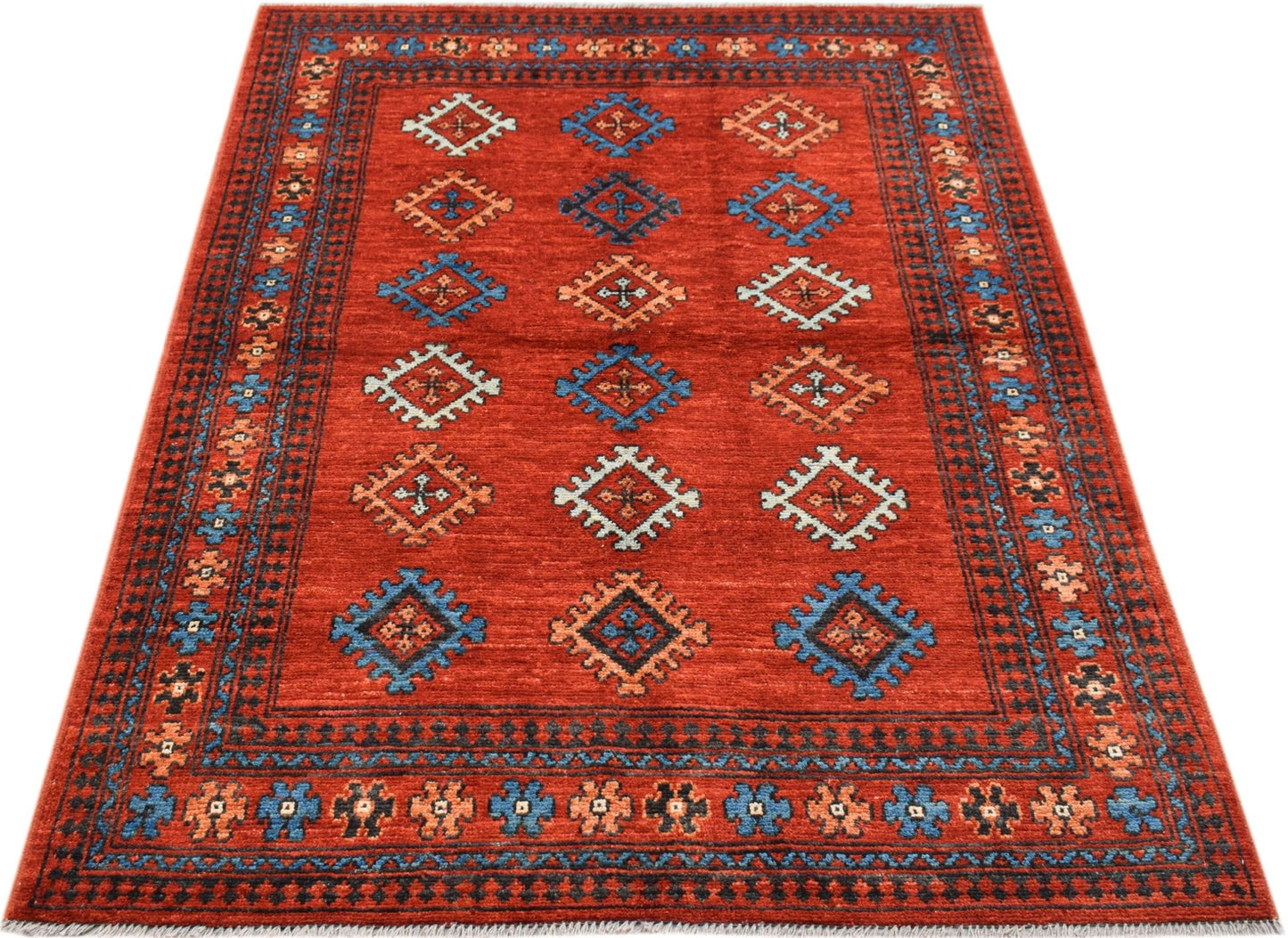 A handwoven Afghan Pashm rug featuring a red field with repeating geometric motifs.