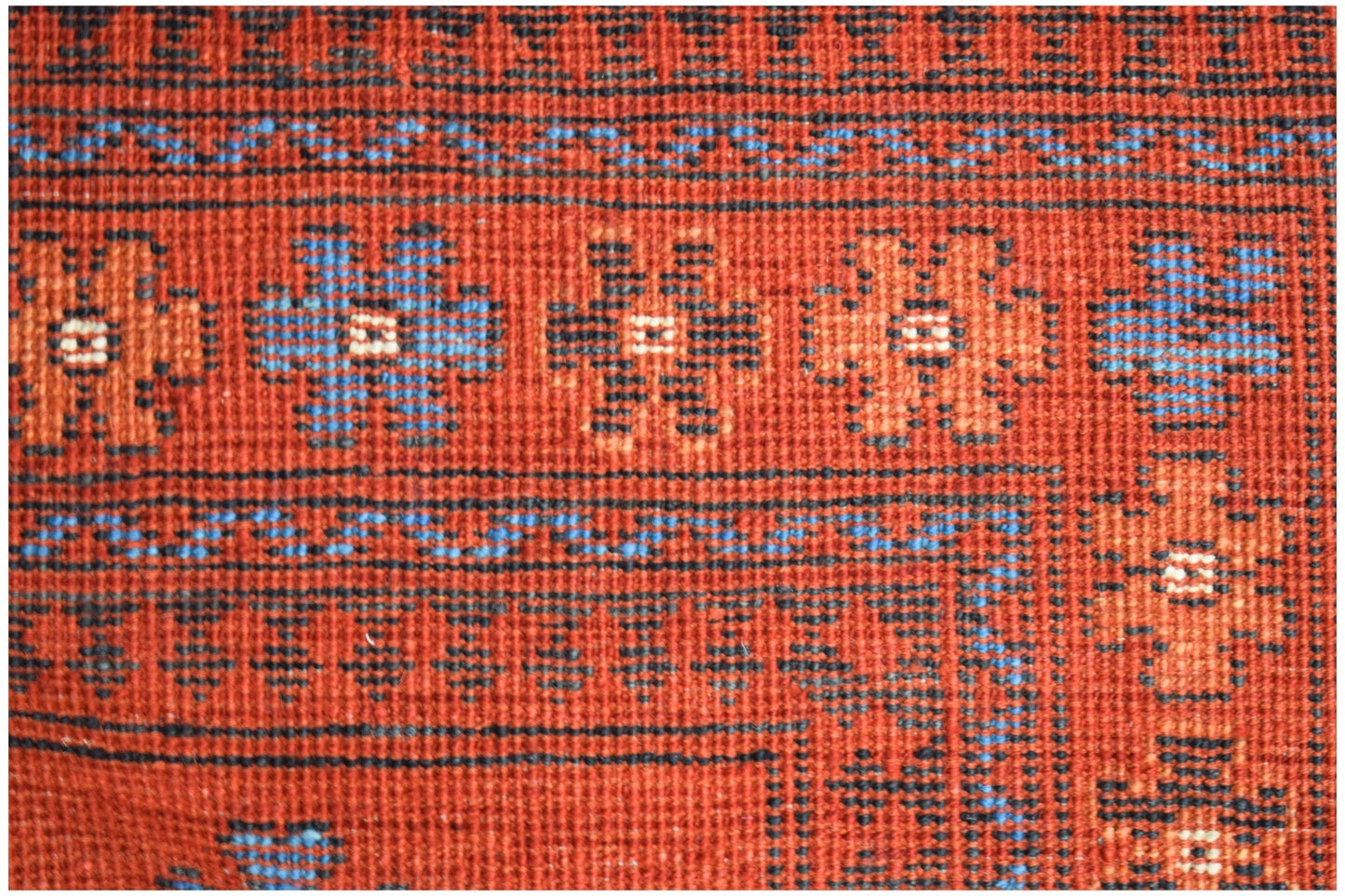 A close-up of a handwoven Afghan wool rug featuring geometric floral patterns in red and blue.