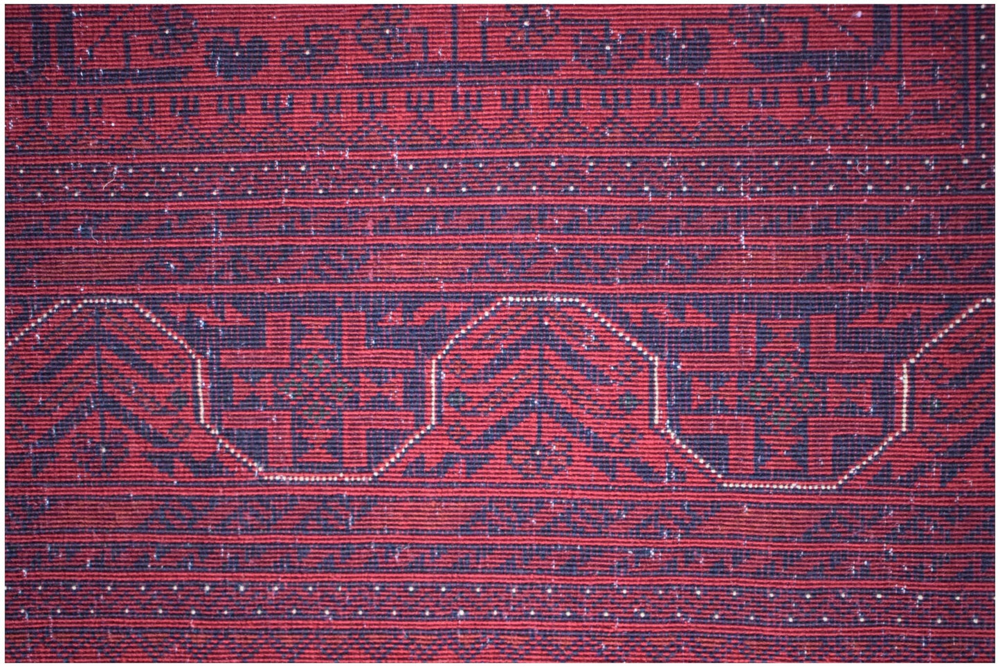 A close-up of an Afghan Biljik rug featuring intricate geometric patterns in deep red and blue.