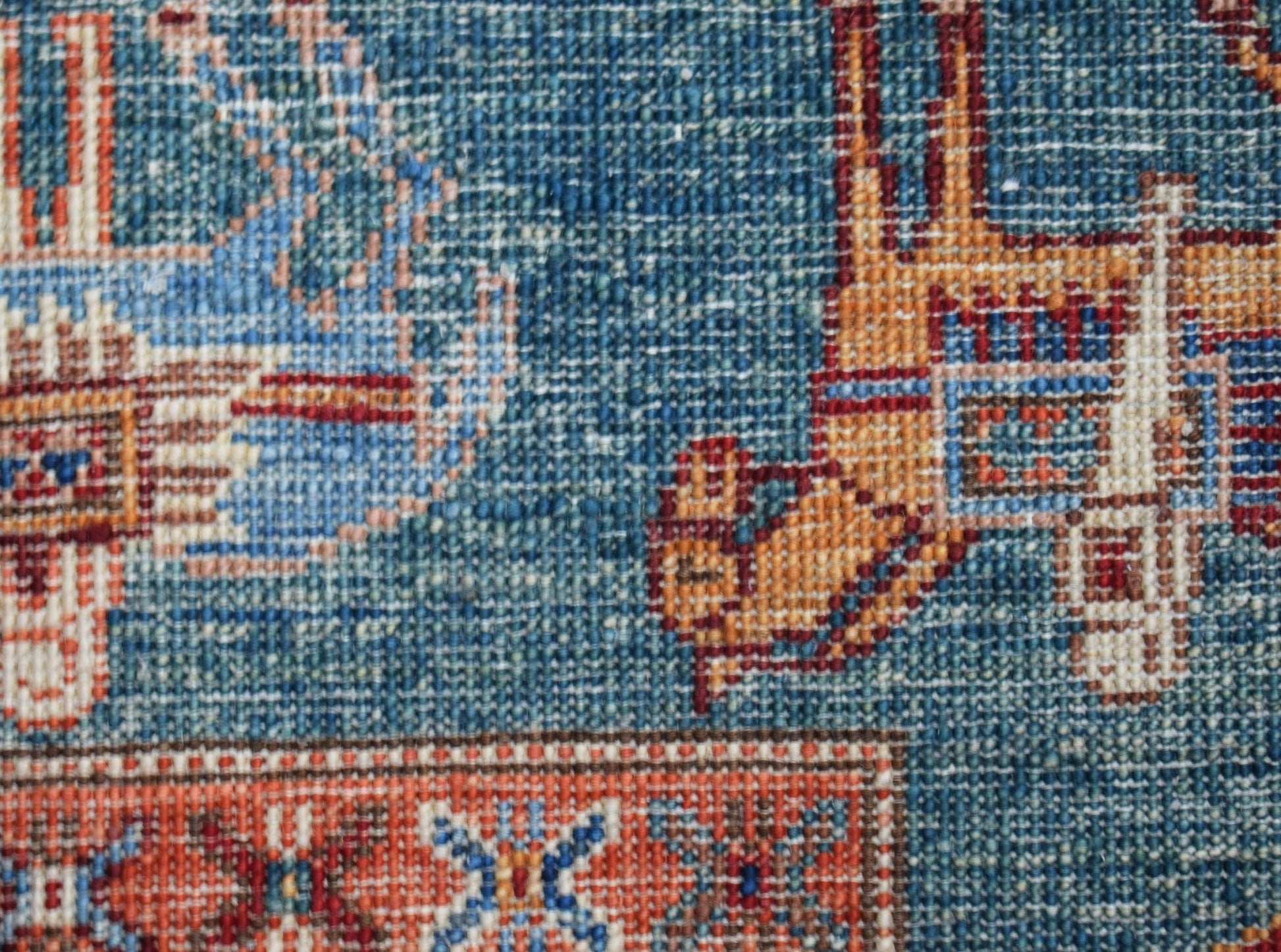 A close-up of a handwoven Afghan Chobi rug featuring intricate geometric patterns in blue and orange.
