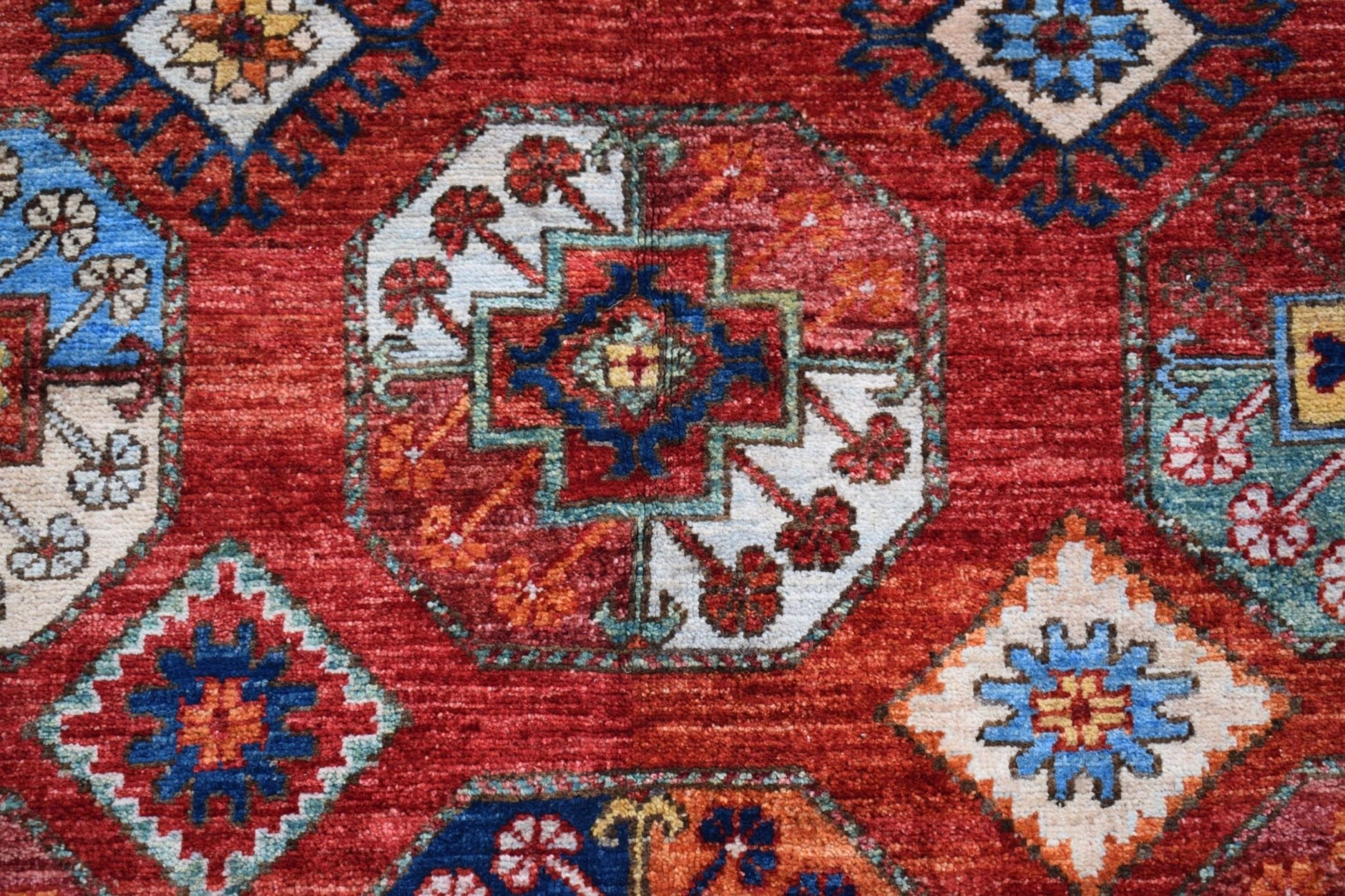 A handmade Afghan Chobi rug featuring a geometric pattern of octagons in red, blue, and cream.