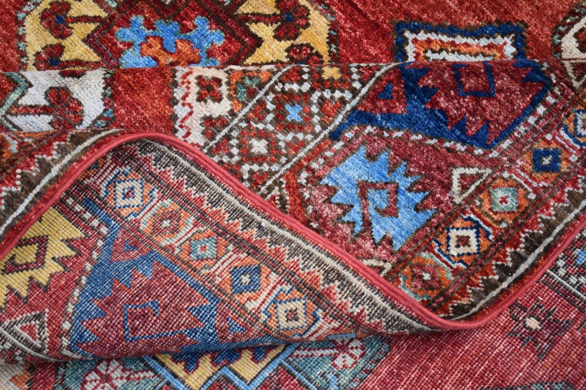 A handmade Afghan Chobi rug featuring a traditional geometric pattern in red, blue, and yellow.