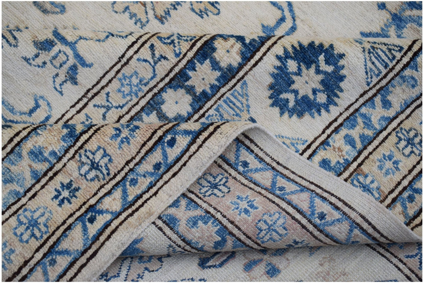 A folded Afghan Super Kazakh wool rug featuring traditional blue floral motifs on a cream background.
