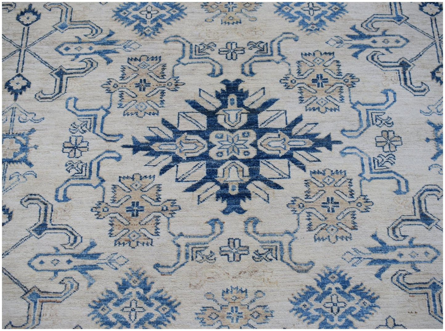 An Afghan Super Kazakh rug featuring a central blue geometric medallion on a cream wool background.