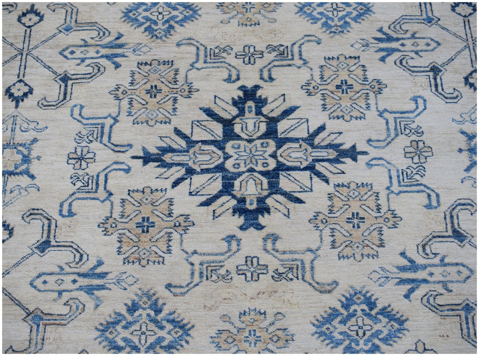 An Afghan Super Kazakh rug featuring a central blue geometric medallion on a cream wool background.