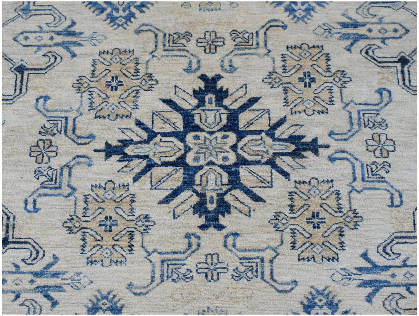 Handmade Afghan Super Kazakh rug featuring a central blue geometric medallion on a cream field.