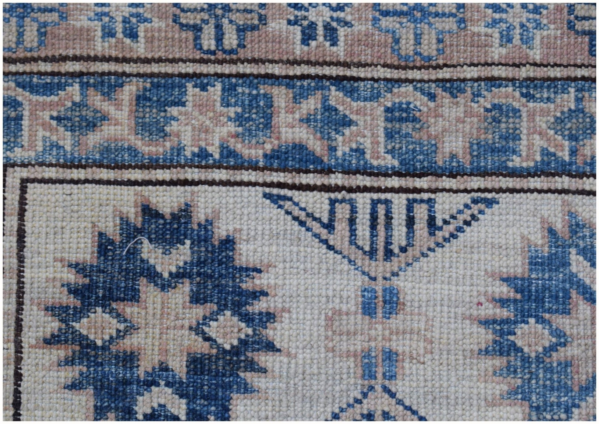 A close-up of an Afghan Super Kazakh rug featuring traditional blue and beige geometric motifs.