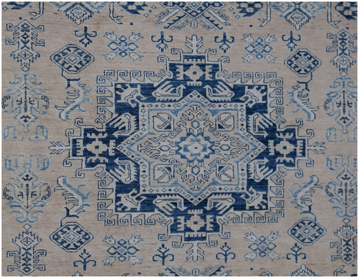 A handmade Afghan Super Kazakh rug featuring a central blue geometric medallion on a beige field.