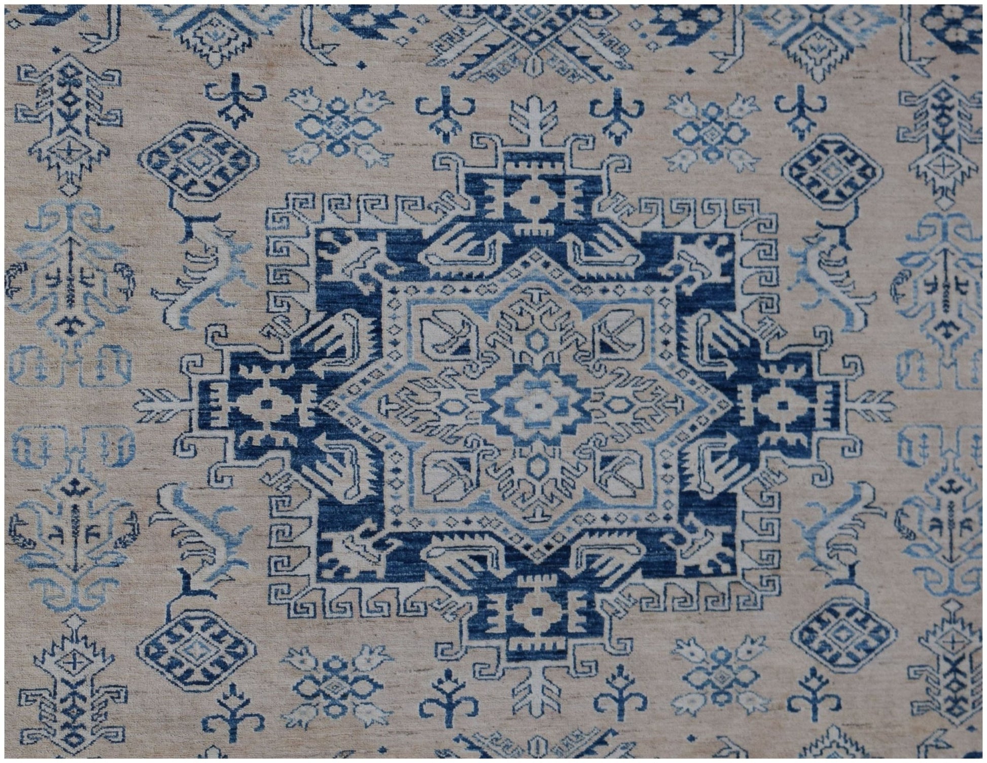 A handmade Afghan Super Kazakh rug featuring a central blue geometric medallion on a beige field.