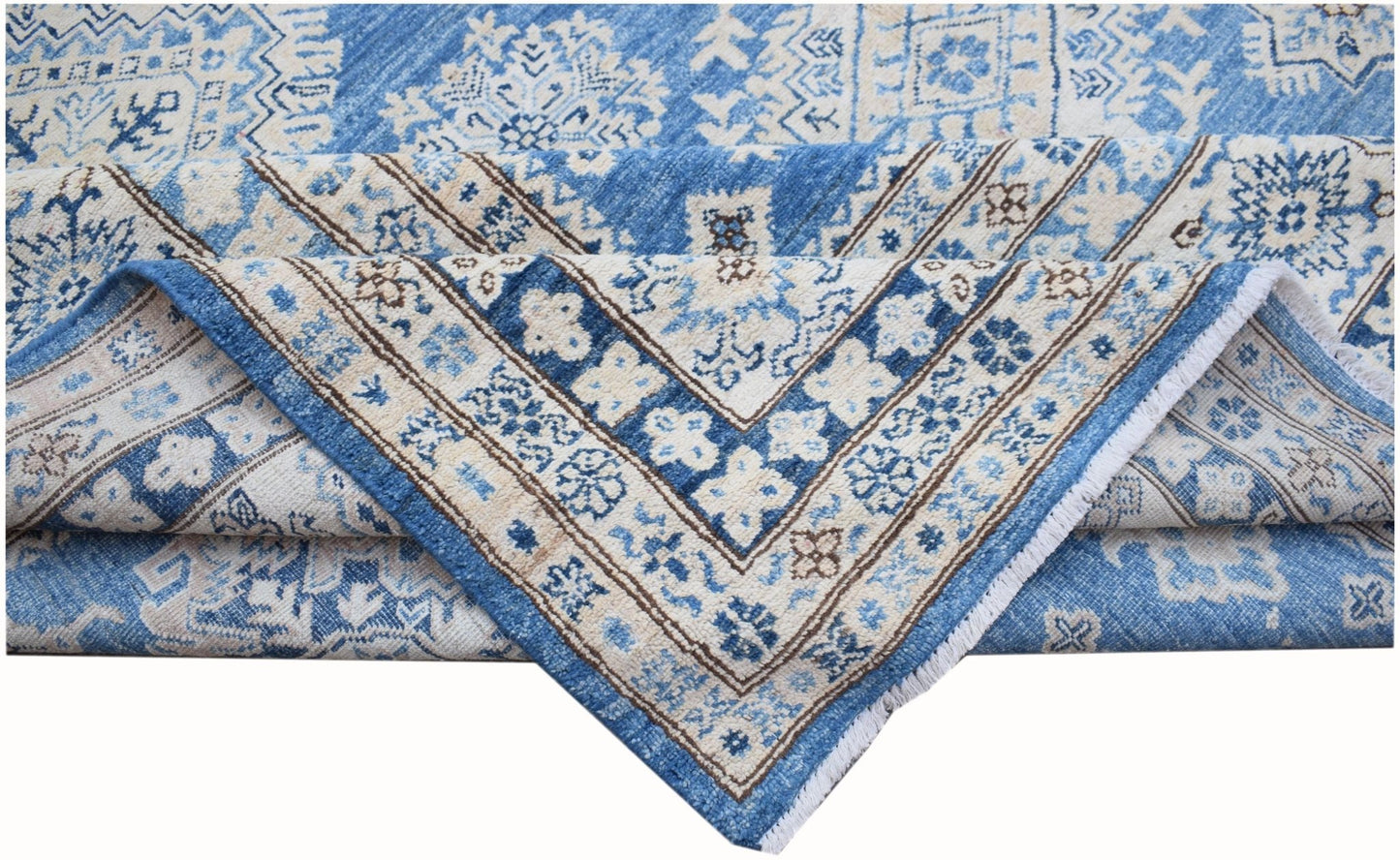 A folded Afghan Super Kazakh rug featuring traditional blue and cream geometric patterns.