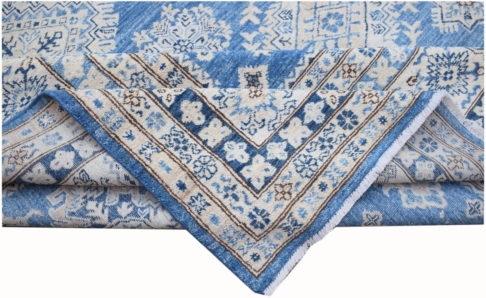 A folded Afghan Super Kazakh rug featuring traditional blue and cream geometric patterns.