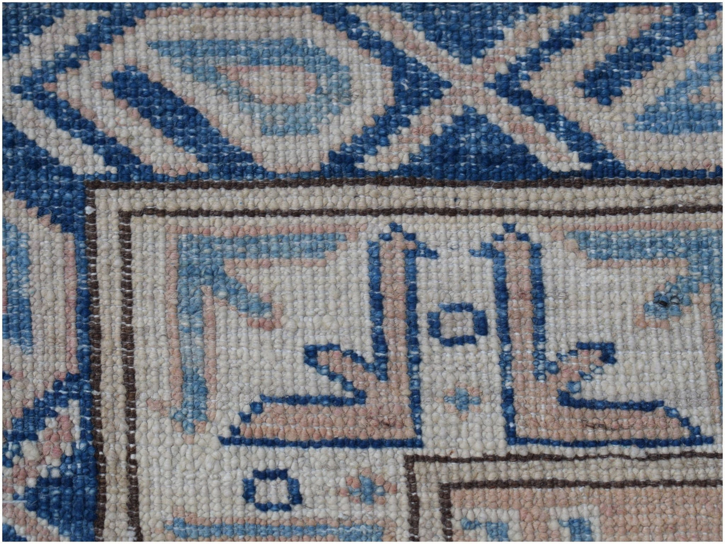 A close-up of an Afghan Super Kazakh rug featuring intricate blue and beige geometric patterns.