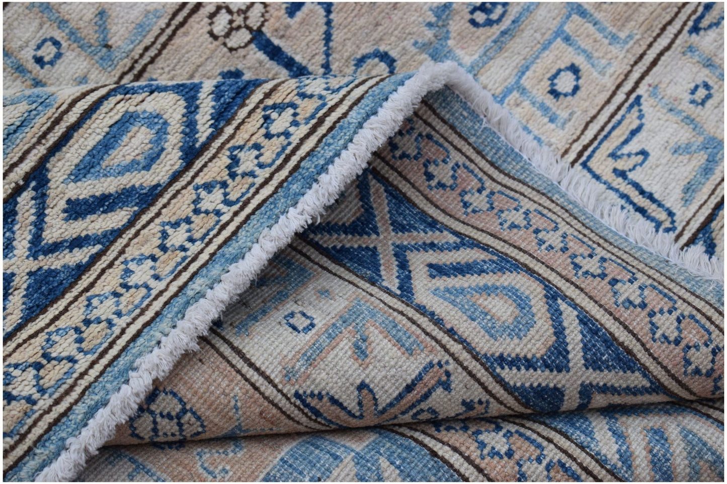 A folded Afghan Super Kazakh rug featuring traditional blue and beige geometric patterns.