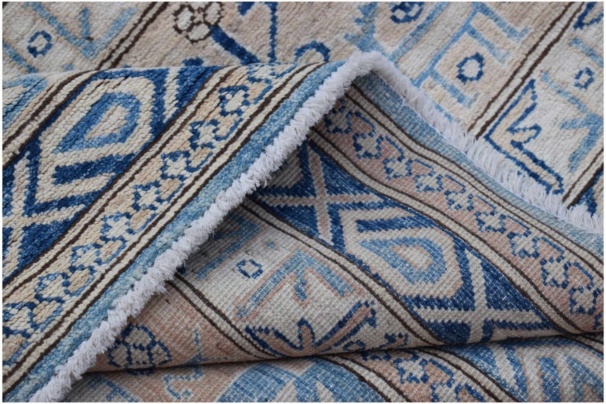 A folded Afghan Super Kazakh rug featuring traditional blue and beige geometric patterns.