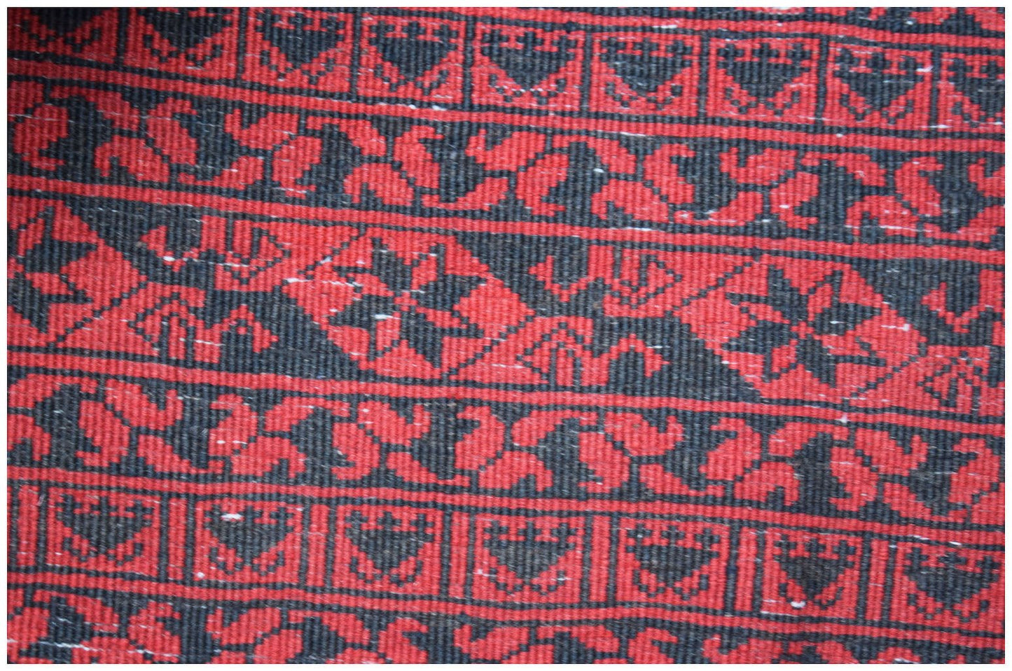A vintage Afghan Turkmen rug featuring repeating geometric and floral patterns in red and black.