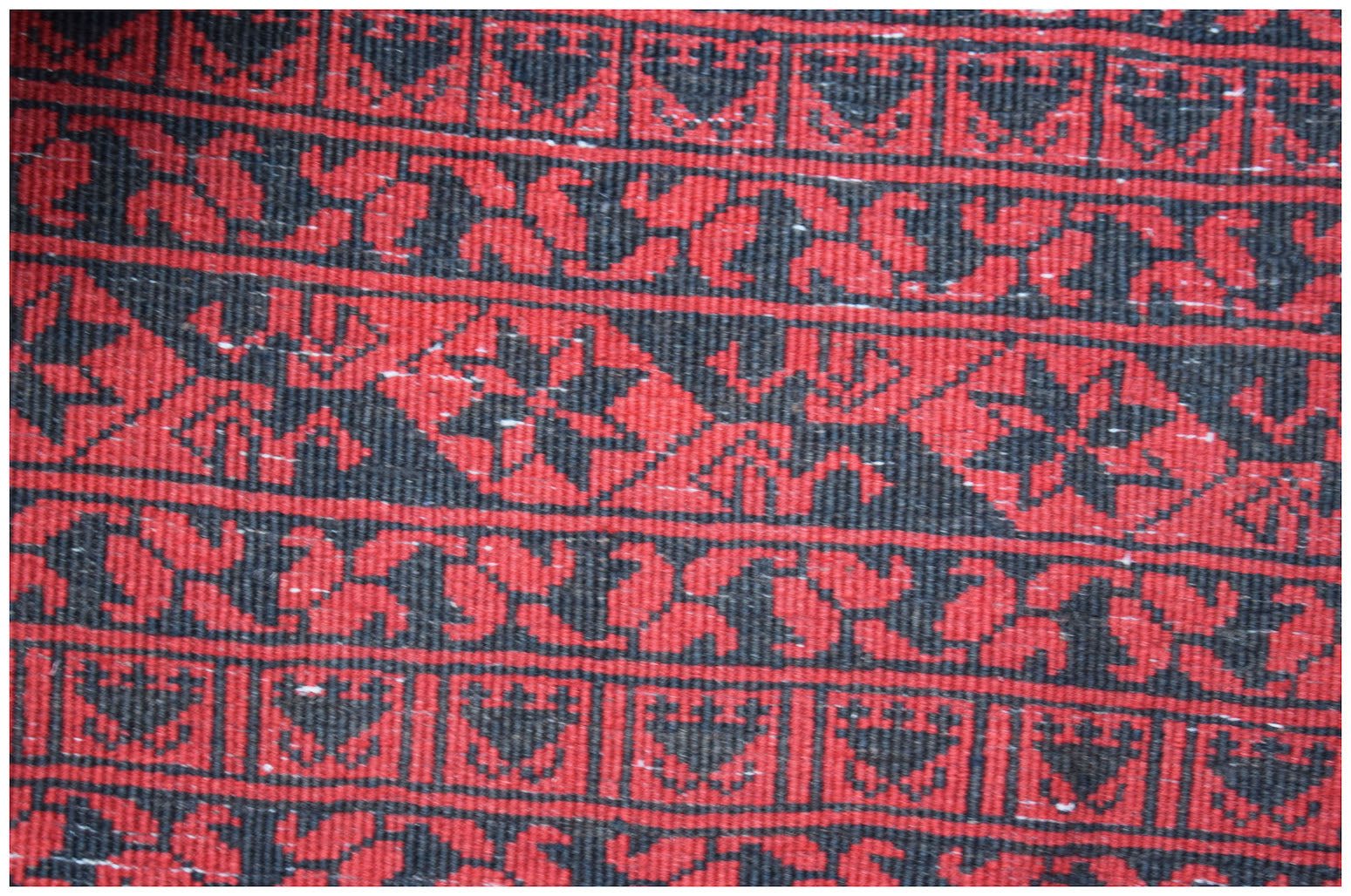 A vintage Afghan Turkmen rug featuring repeating geometric and floral patterns in red and black.