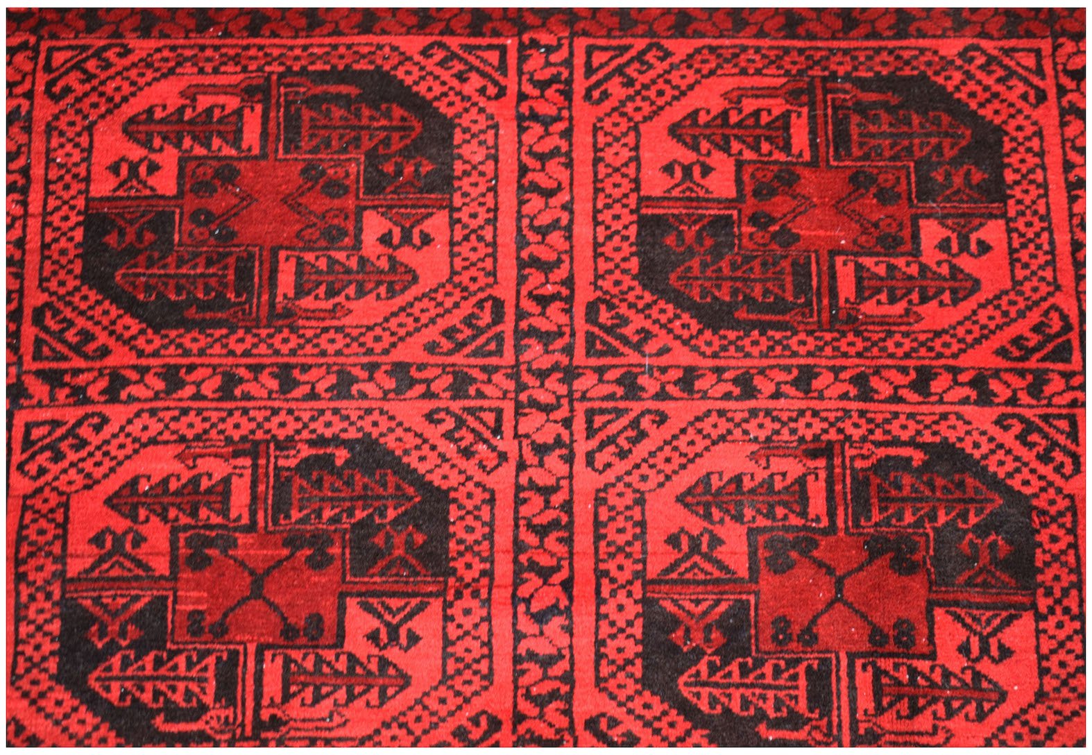 A vintage Afghan Turkmen rug featuring a repeating black and red geometric gul pattern.