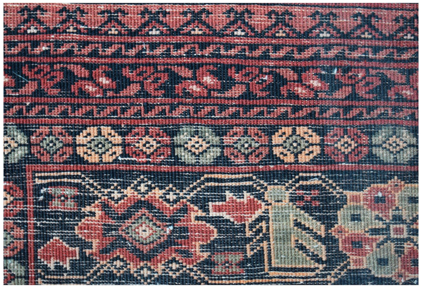 A close-up of a vintage Afghan Turkmen rug featuring geometric patterns in red, black, and green.