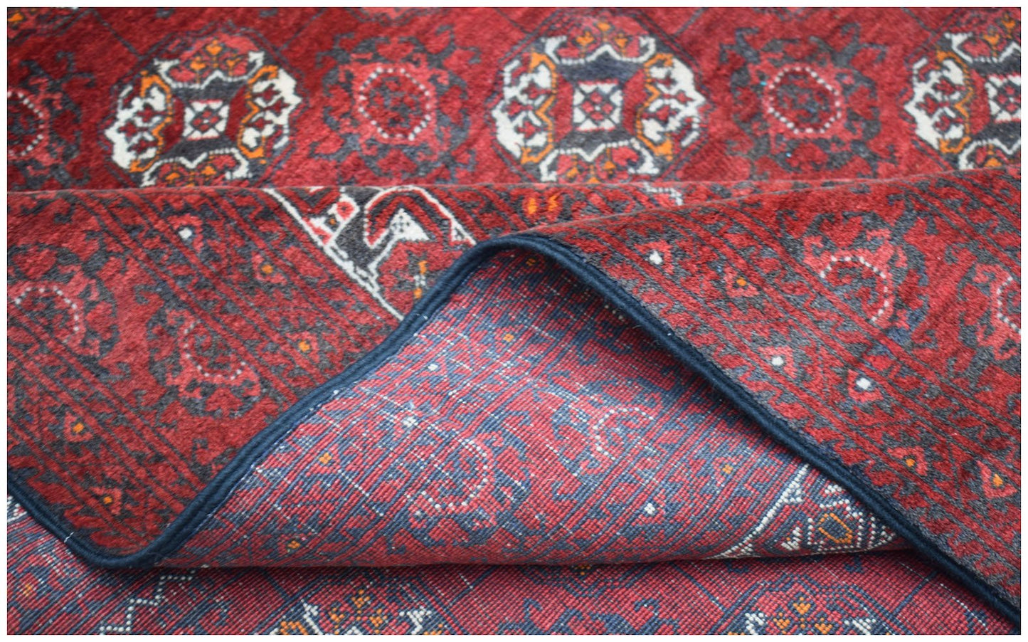 A vintage Afghan Turkmen wool rug featuring a repeating geometric pattern in red and dark grey.
