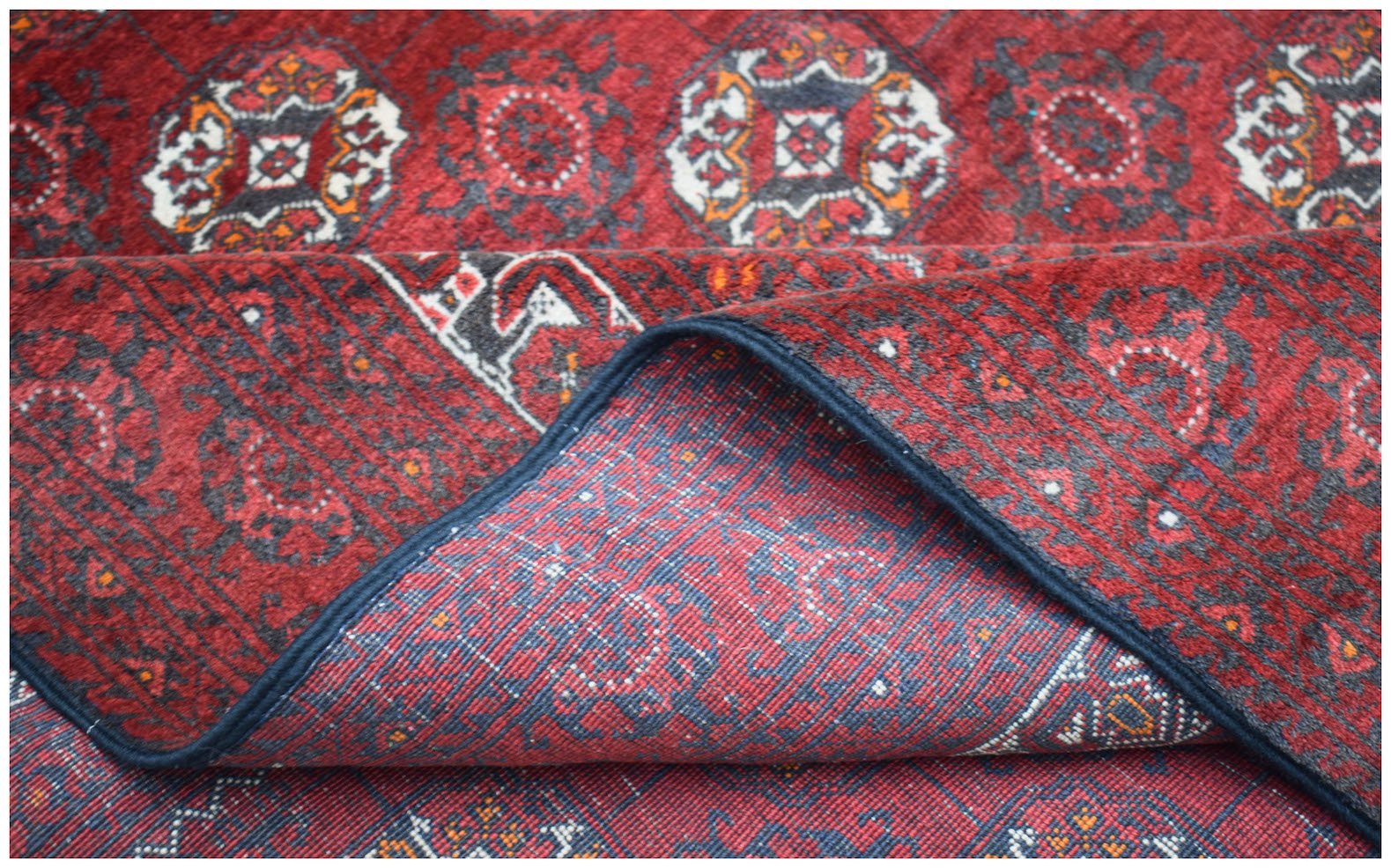 A vintage Afghan Turkmen wool rug featuring a repeating geometric pattern in red and dark grey.