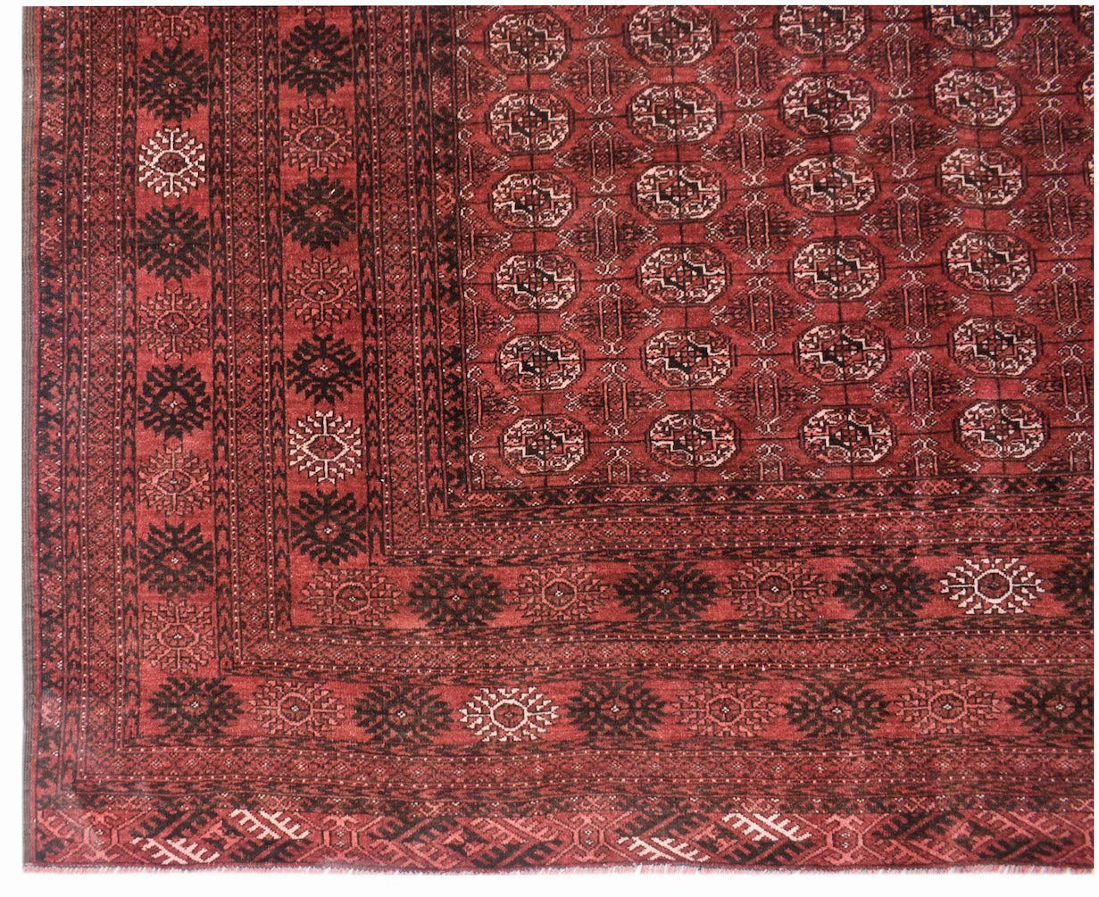 A vintage Afghan Turkmen rug featuring a deep red field with repeating geometric elephant foot motifs.