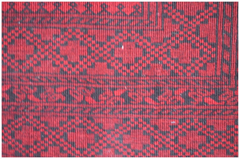A vintage handmade Afghan Turkmen rug featuring a repeating geometric pattern in red and black.