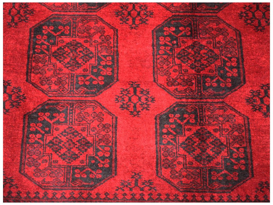 A vintage Afghan Turkmen rug featuring a repeating black geometric pattern on a deep red background.