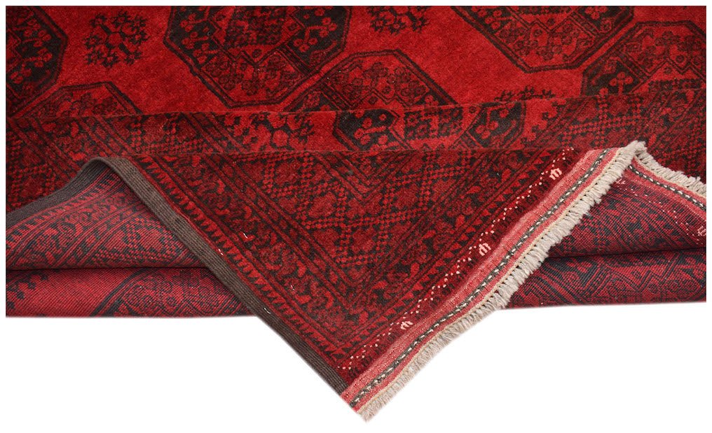 A vintage Afghan Turkmen rug with a red field and black geometric patterns, showing a folded corner.