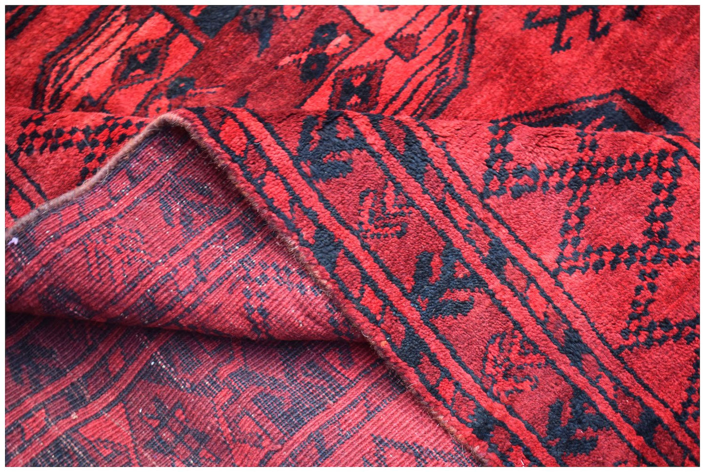 A vintage handmade Afghan Turkmen wool rug featuring a red background with black geometric motifs.