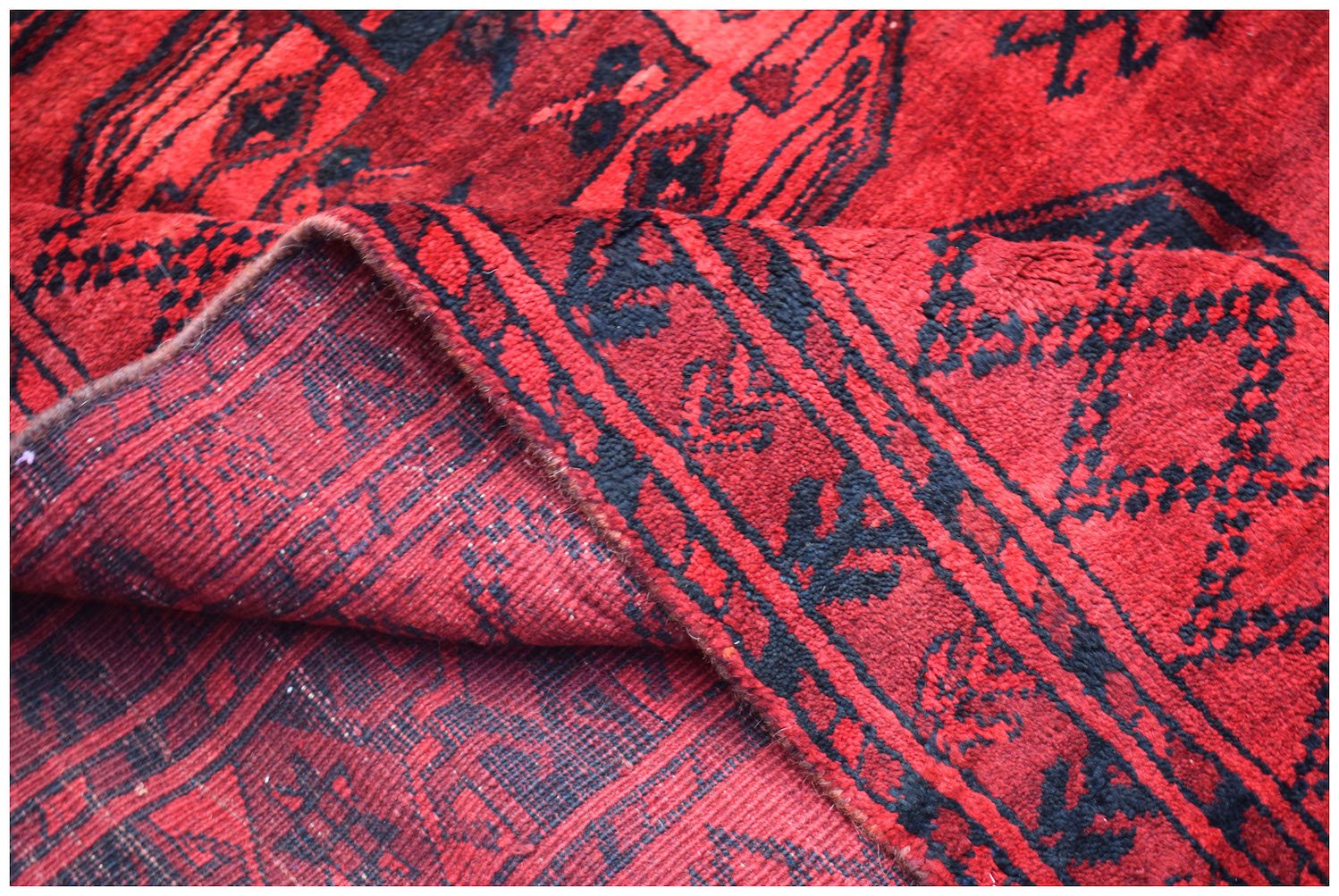 A vintage handmade Afghan Turkmen wool rug featuring a red background with black geometric motifs.