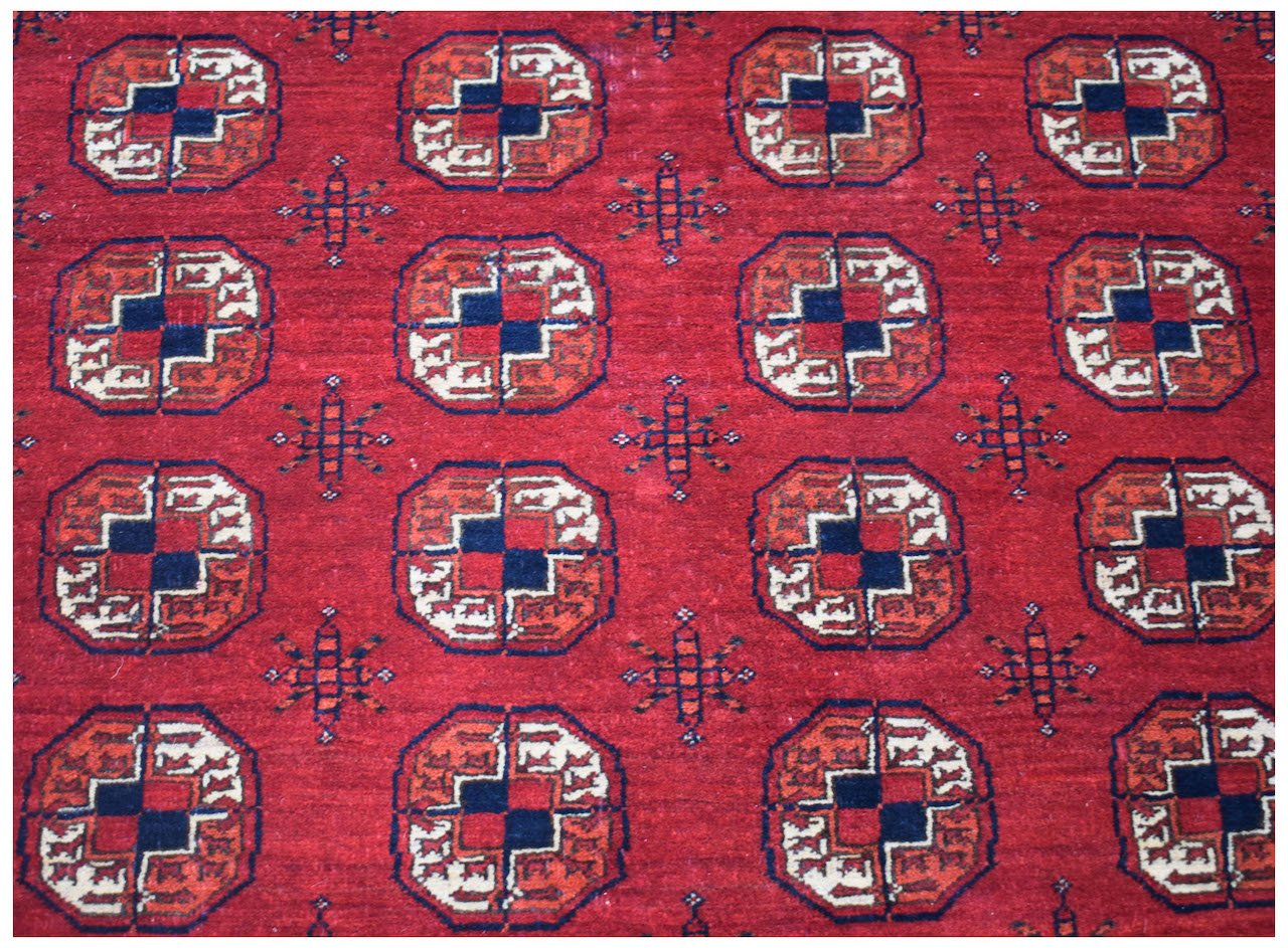 A vintage Afghan Turkmen wool rug featuring a repeating red and navy blue elephant foot motif.