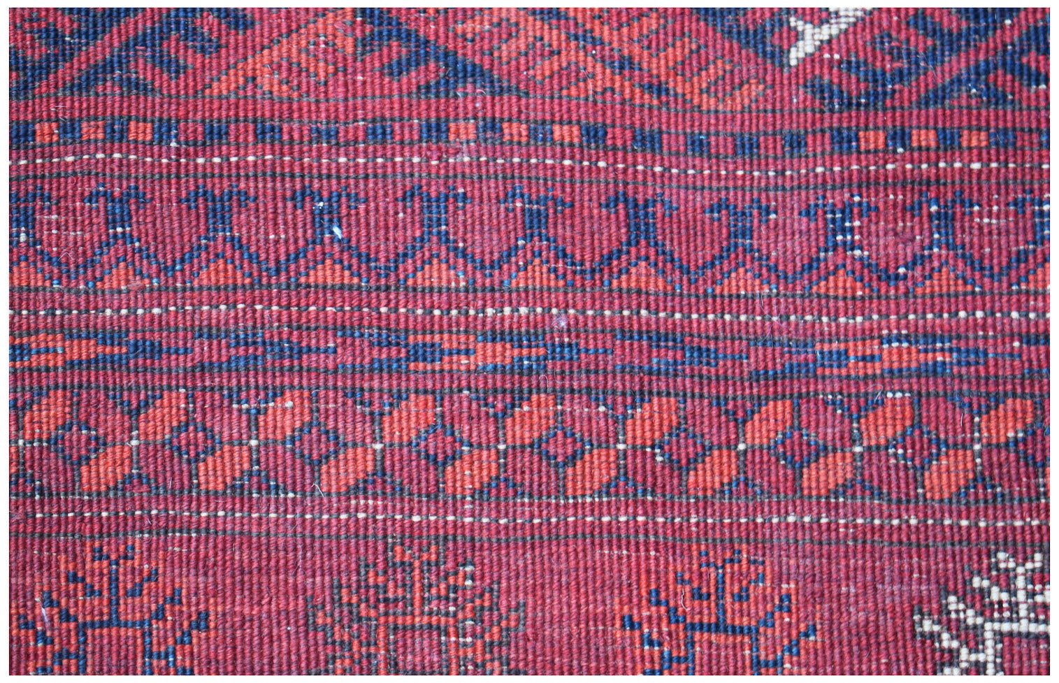A close-up of a vintage handmade Afghan Turkmen wool rug featuring geometric patterns in red and blue.