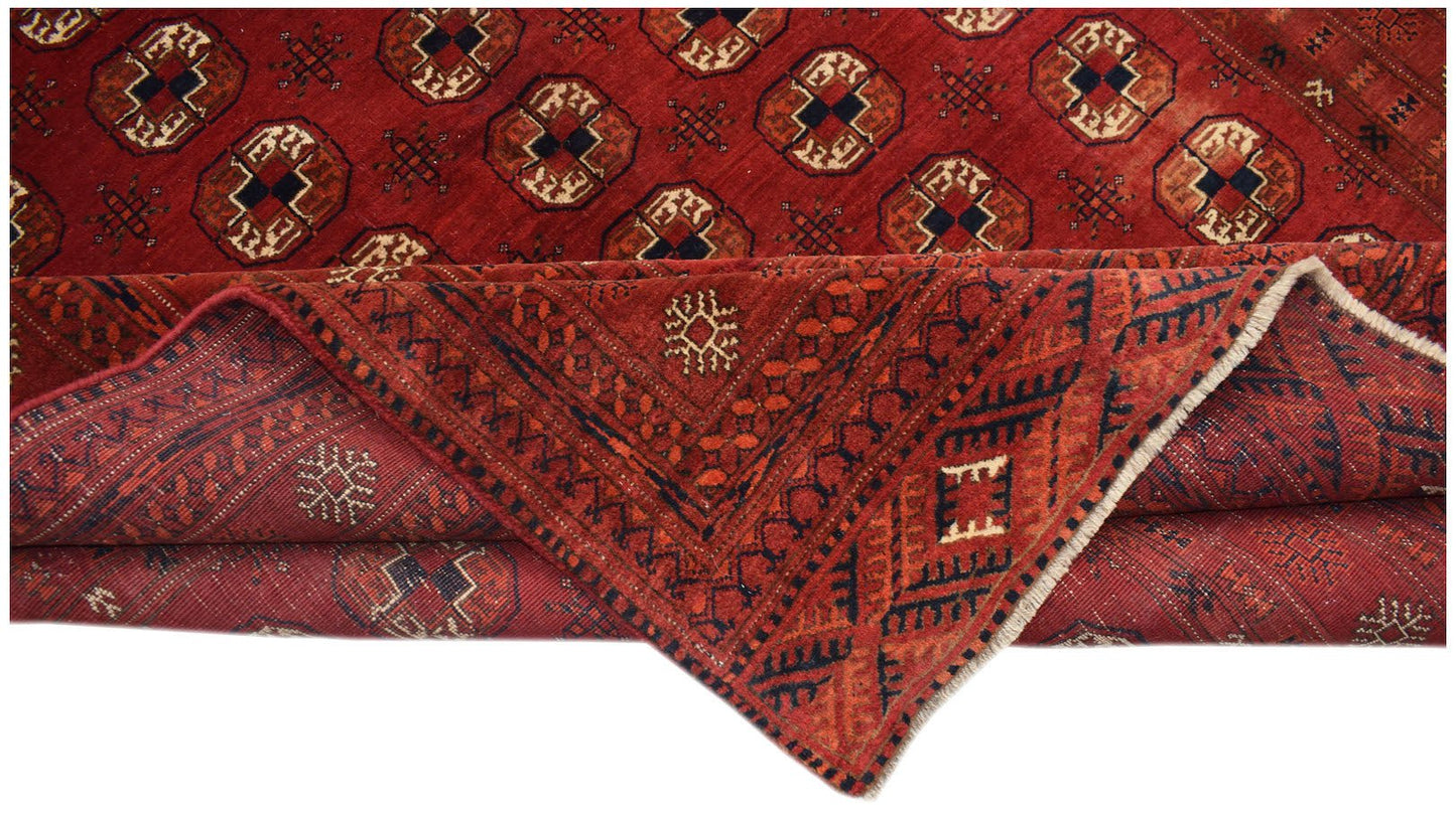 A vintage handmade Afghan Turkmen rug featuring a red field with repeating elephant foot motifs.
