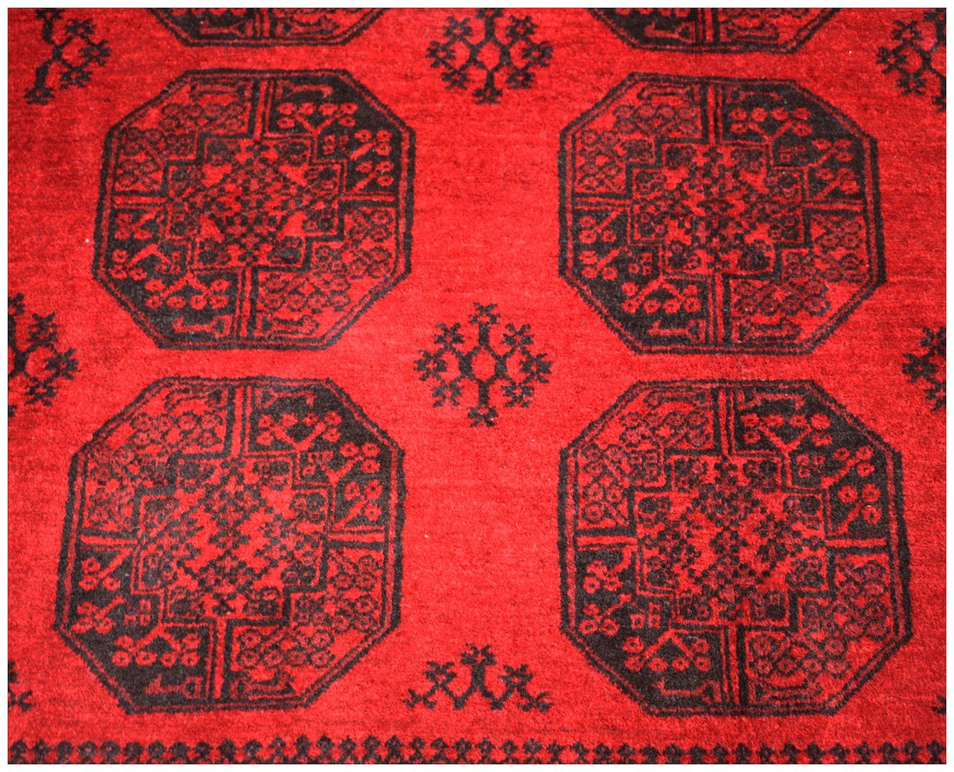 A vintage Afghan Turkmen rug featuring a repeating black elephant foot motif on a red wool field.
