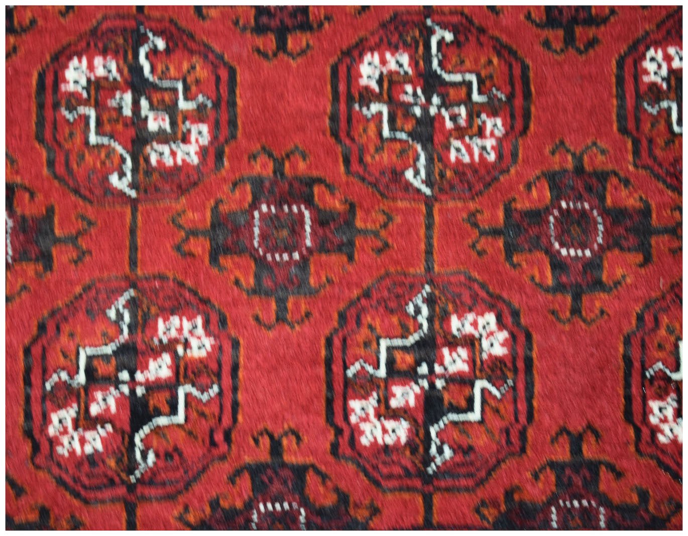 A vintage Afghan Turkmen rug featuring a repeating red and black geometric elephant foot motif.