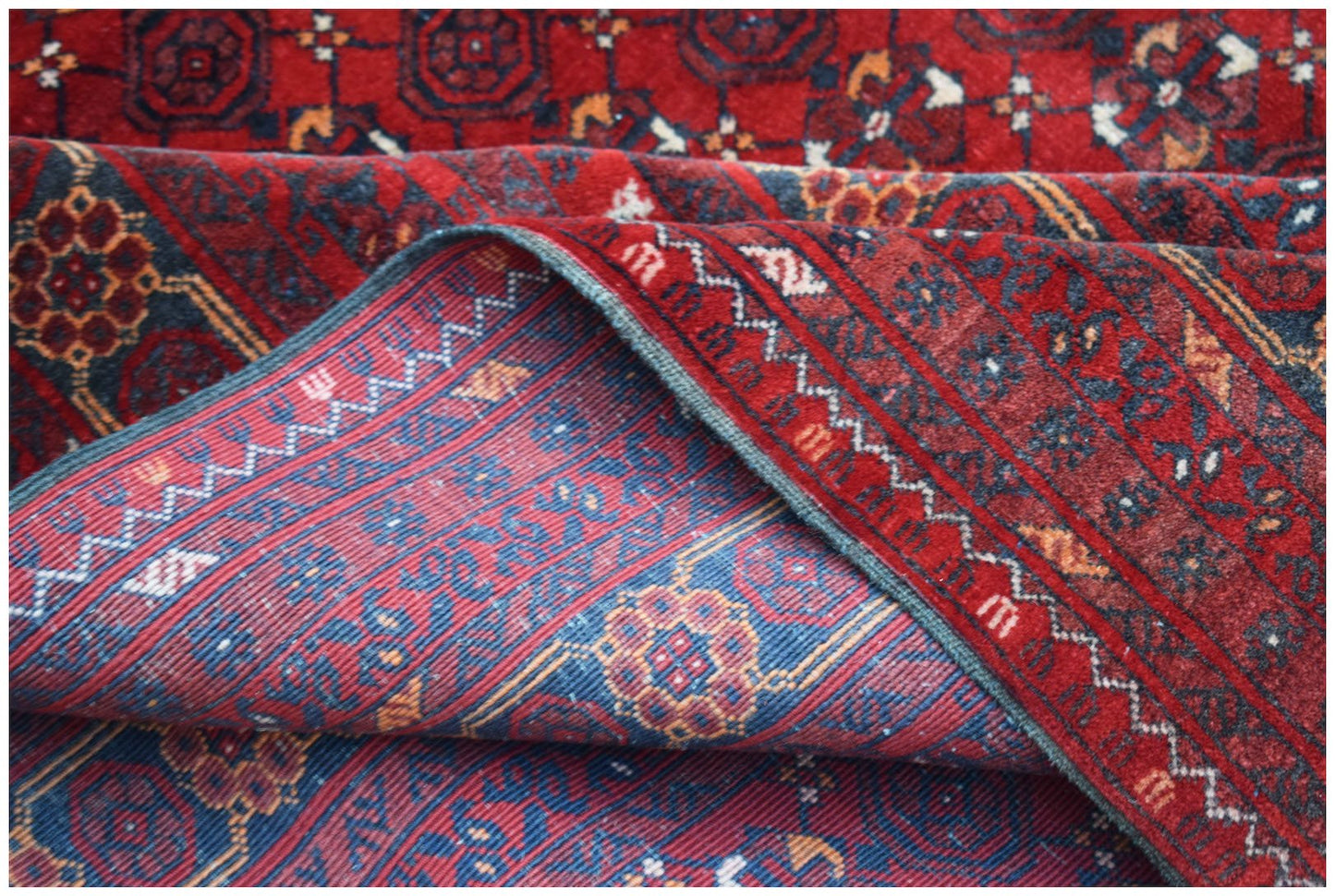 A vintage handmade Afghan Turkmen wool rug featuring a red geometric elephant foot motif.