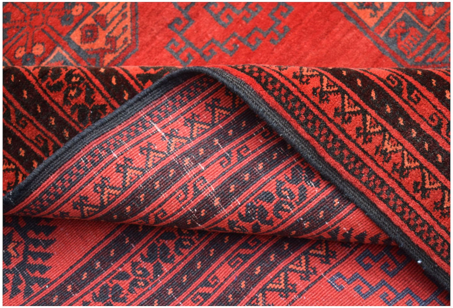 A vintage Afghan Turkmen wool rug featuring a red background with geometric elephant foot motifs.