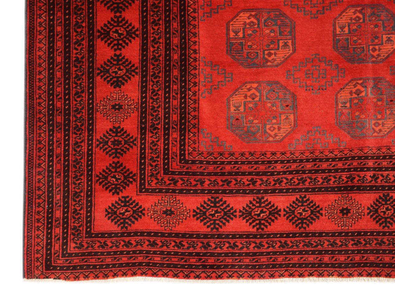 A vintage Afghan Turkmen rug featuring a red field with repeating dark elephant foot motifs.